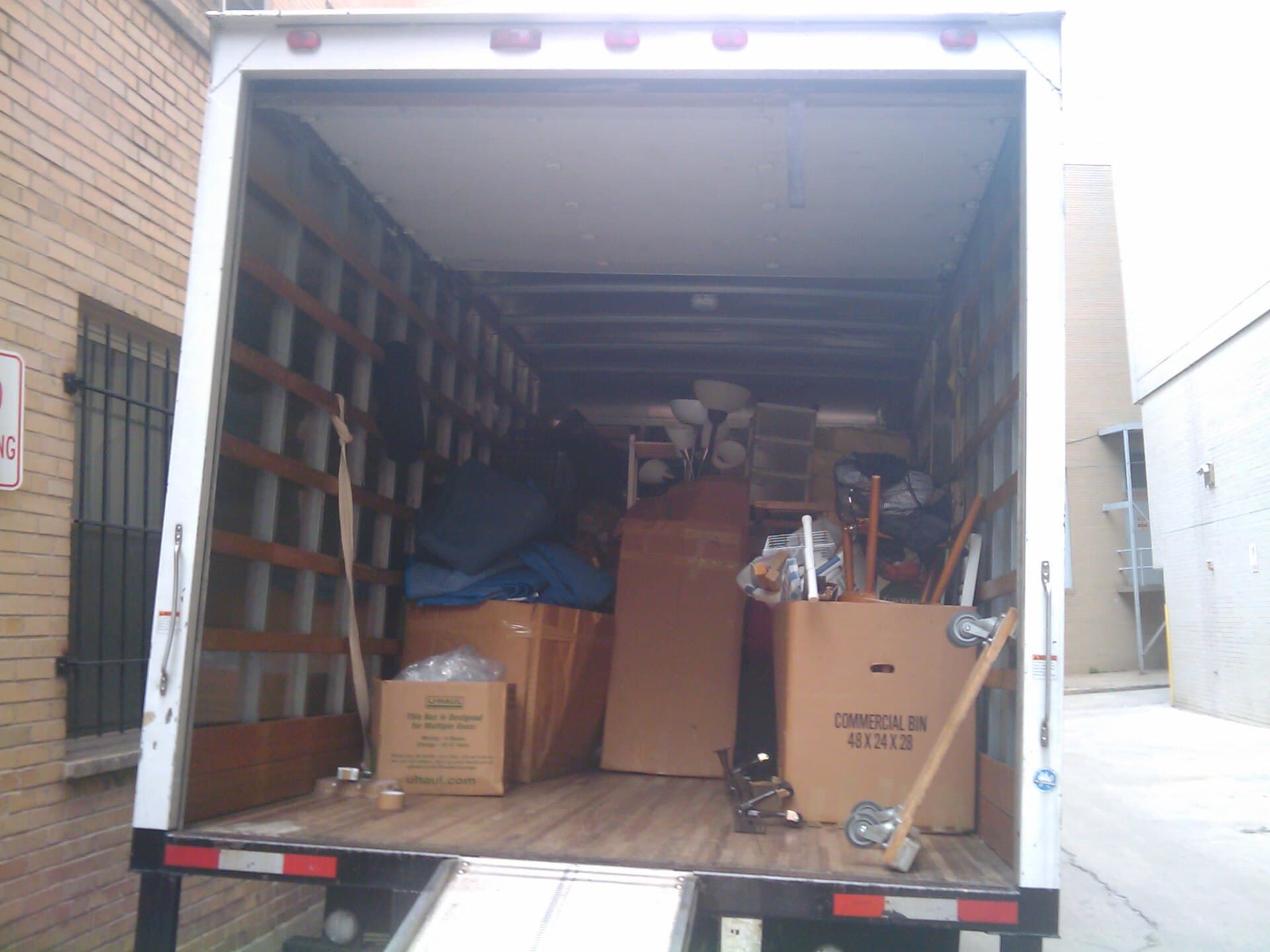 Workers unloading cardboard moving boxes from a truck at a suburban house