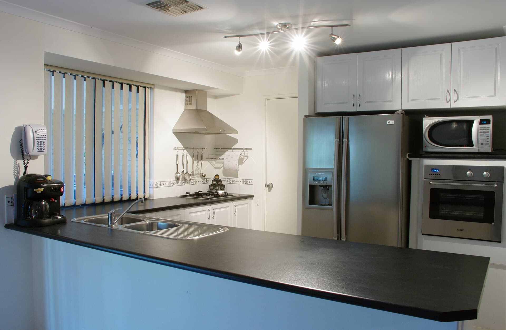 A modern Australian kitchen with white cabinets, a gas cooktop, stainless-steel fridge and black benchtop.